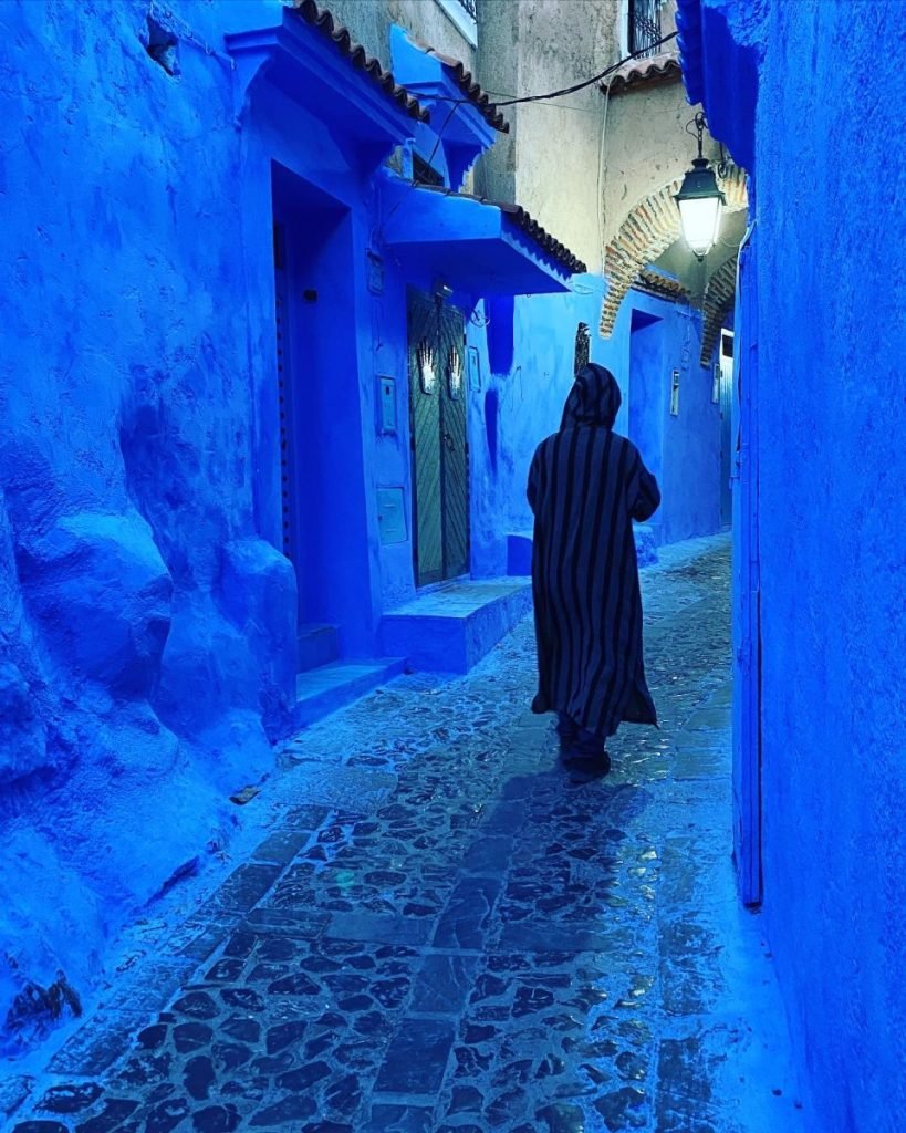 Trin wearing his djellaba as he walks down a blue Chefchaouen street in the evening