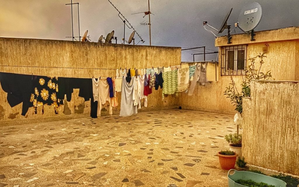 Cement rooftop with laundry hanging on lines and satellite dishes pointing east.