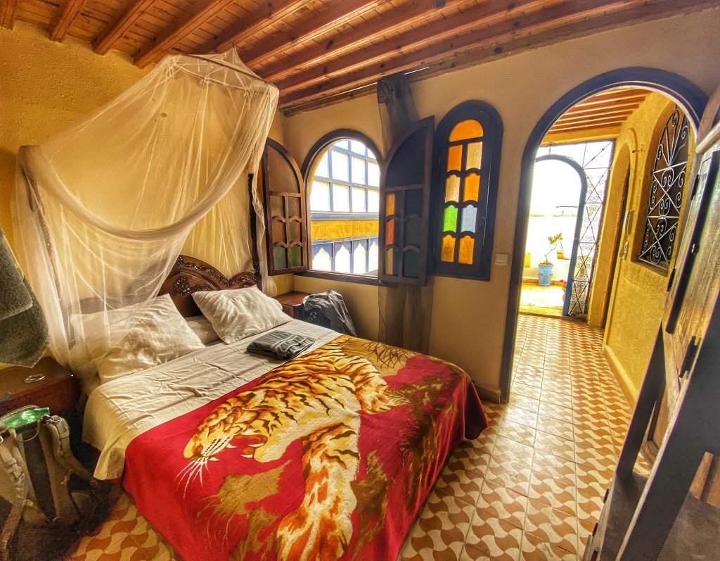 Beautifully colorful room in Morocco with a door to the balcony and mosquito netting for the bed.