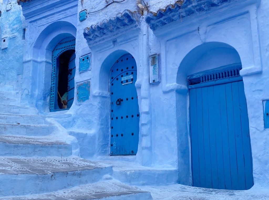 Three blue doors set in blue painted cement beside blue stairs.