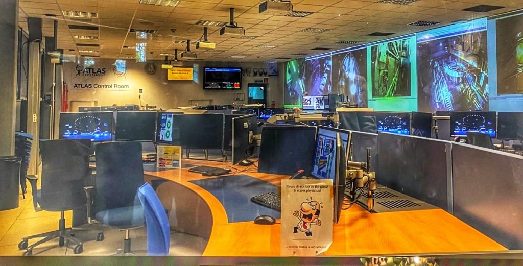 The Atlas Control Room filled with monitors and large screen projectors. One physicist sits at his desk.