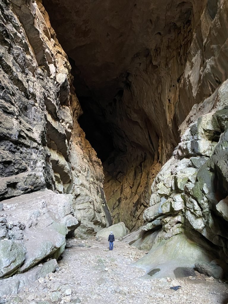 Trin standing in front of a massive opening into a cave.