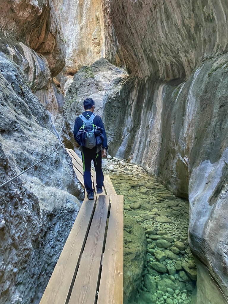 Trin walking on a small planked pathway over water through a narrow canyon in Estrecho del Parrizal.