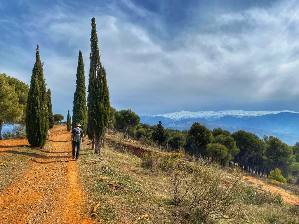 Trin on the red dirt trail heading east out of Granada on the ridge-line. Snow capped mountains are in the distance.