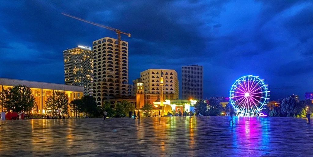 Skanderbeg Square at night, the lights of the Ferris wheel reflect off the marble square.