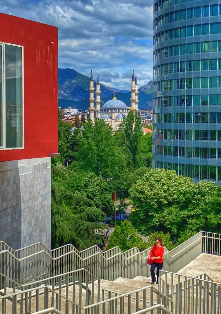 View of the tree filled city from the top of the Pyramid of Tirana. The mosque and mountains are visible in the background. 