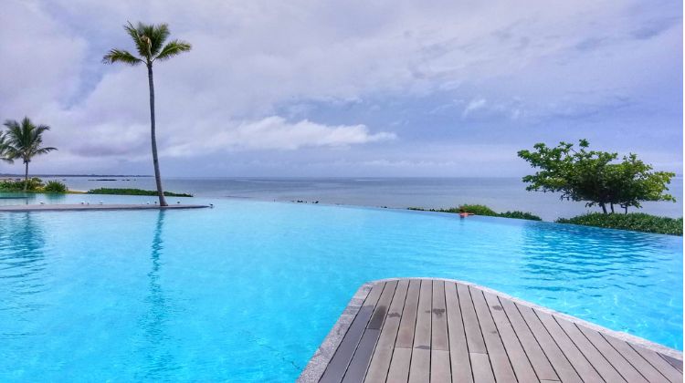 Massive Negative edge pool with blue water and palm trees looking over the ocean