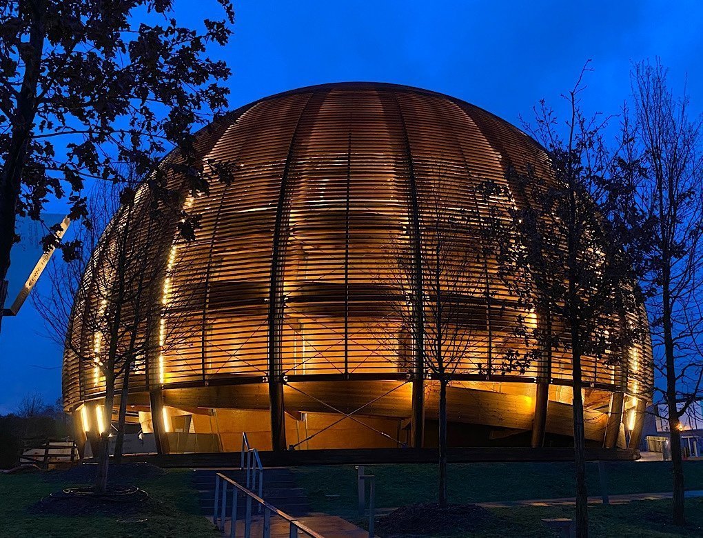 A dome building at CERN lit up against a dark blue morning sky